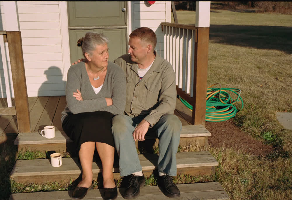 A couple in their sixties sitting on their back porch steps in early September light